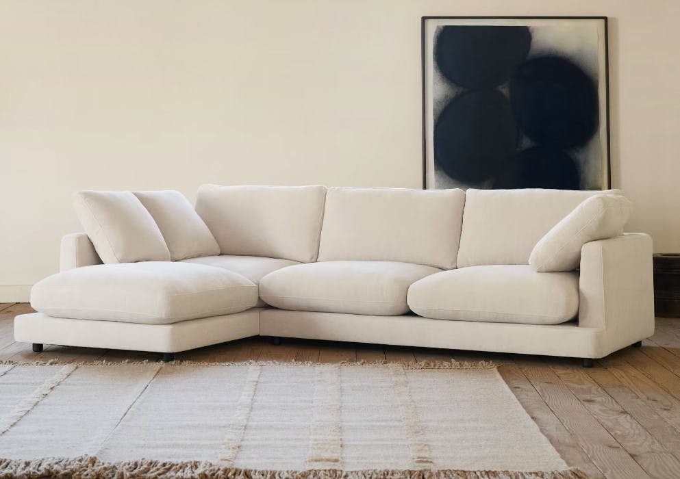 beiges Sofa L-Form links in Wohnzimmer mit Holzboden und Teppich