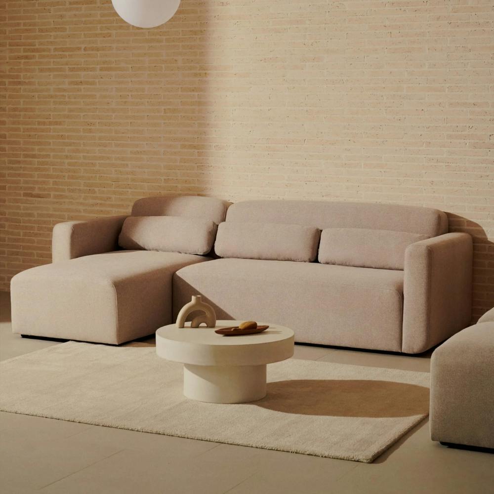 beiges Polster Sofa L-Form links in Wohnzimmer mit Teppich und hellem Couchtisch